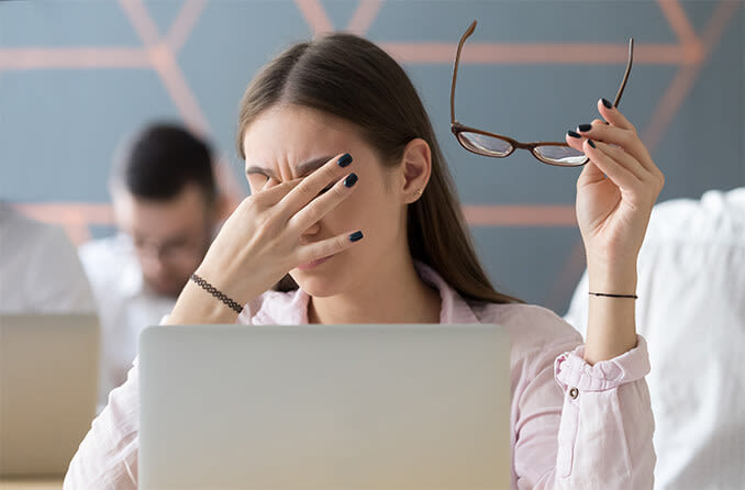 Office worker rubbing eyes in front of computer